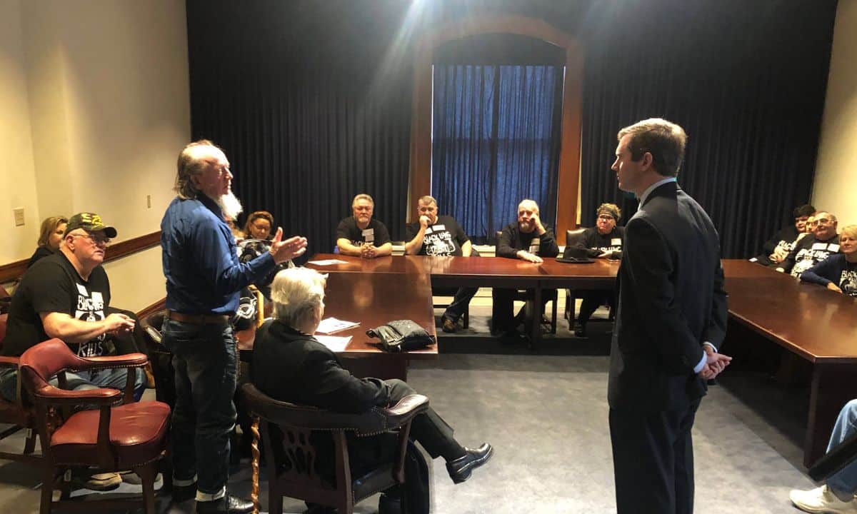 A picture of Wes Addington, center, in the center of a U-shaped table setup, talking with miners.
